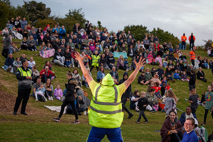 A clown in high-vis costume raises his hands to the onlooking crowd